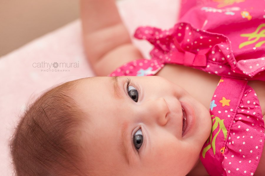 An adorable baby with beautiful eyes smiling on her bed - Captured by a Glendale Lifestyle Baby Photographer, Cathy Murai Photography