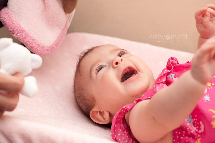 An adorable baby with beautiful eyes smiling and laughing on her bed - Captured by a Glendale Lifestyle Baby Photographer, Cathy Murai Photography