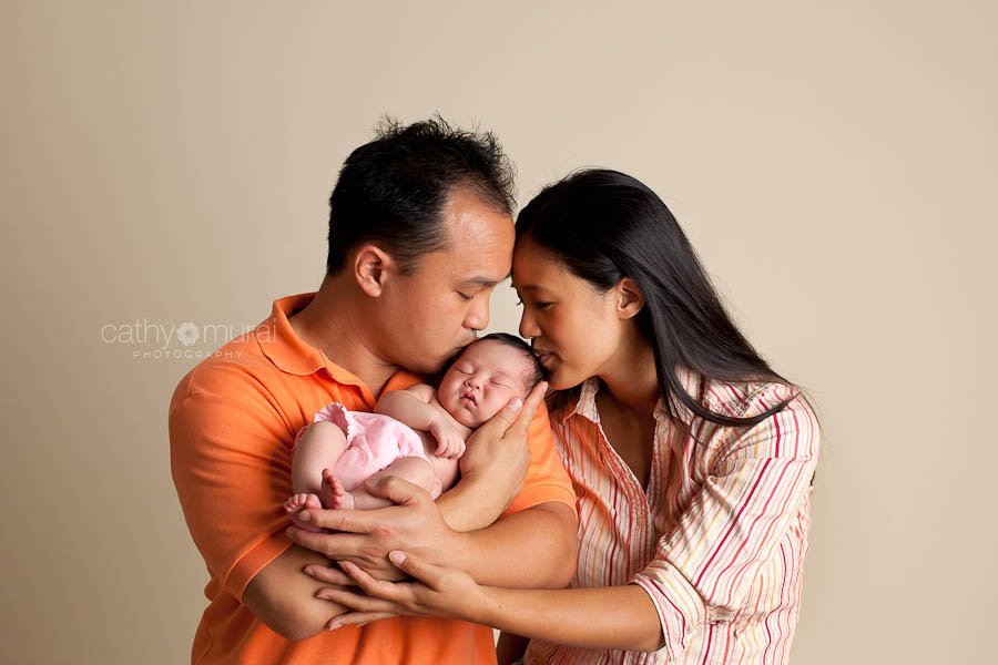 Precious Asian Newborn Baby Girl in a pink diaper sleeping in the family portrait while dad and mom are kissing her head in the picture captured by Pasadena, south Pasadena, Alhambra, San Gabriel Valley Newborn Photographer, Pet Photographer, Family Photographer, Cathy Murai Photography