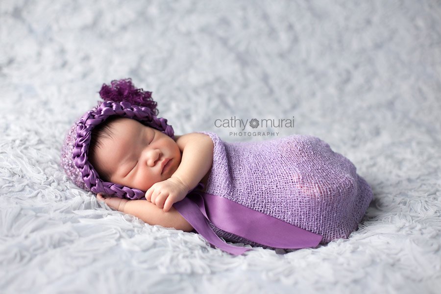 Adorable Asian newborn bab girl wearing a purple bonnet and strech knit wrap