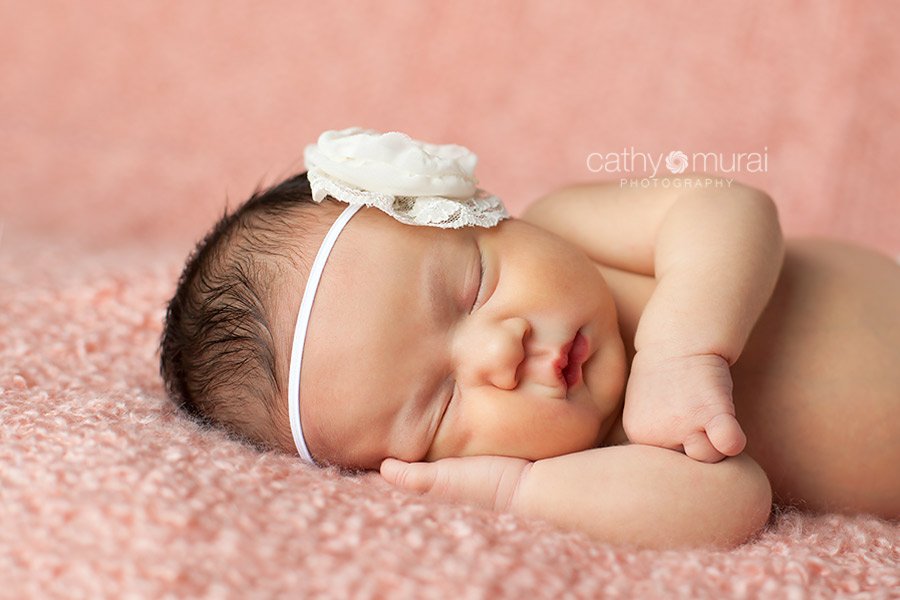 A cute newborn baby girl with chubby cheeks is  wearing a cream diaper cover and headband. She is posing and sleeping on the pink peach backdrop on the beanbag, Cathy Murai Photography, Newborn and Baby Photographer in Alhambra, San Gabriel Valley, and Los angeles Area 