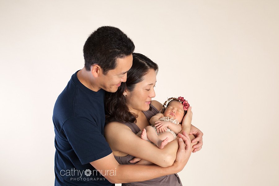 A family portrait of Asian parents and a beautiful 8 day old newborn baby girl wearing the red halo and the cream lace romper.  A family portrait taken in the studio during newborn portrait session, Los Angeles, San Gabriel Valley, Alhambra Newborn Photographer, Cathy Murai Photography