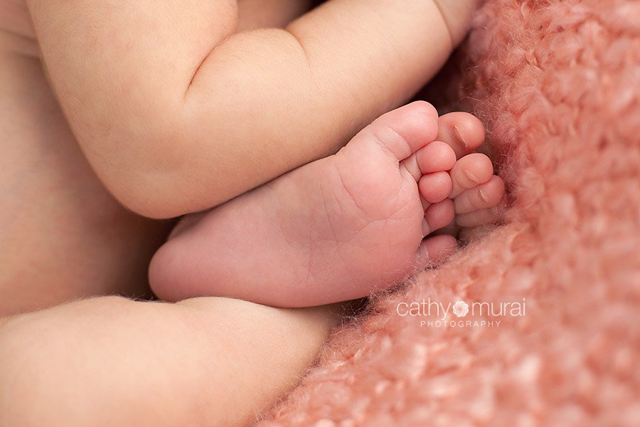 Close up image of baby's feet. A beautiful 8 day old Asian newborn baby girl sleeping necked on the peach pink bean bag blanket, Taco pose, A newborn baby portrait taken in the studio during newborn portrait session by Los Angeles, San Gabriel Valley, Alhambra Newborn Photographer, Cathy Murai Photography