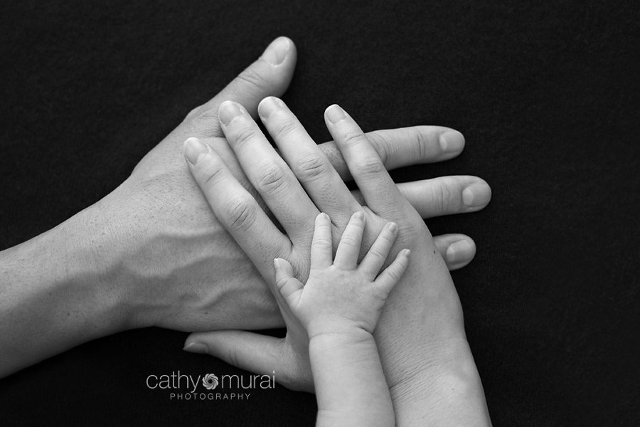Close up black and white image of family's hands.  A baby's tiny hand on her parents' hands. A beautiful 8 day old Asian newborn baby girl. A newborn baby portrait taken in the studio during newborn portrait session by Los Angeles, San Gabriel Valley, Alhambra Newborn Photographer, Cathy Murai Photography