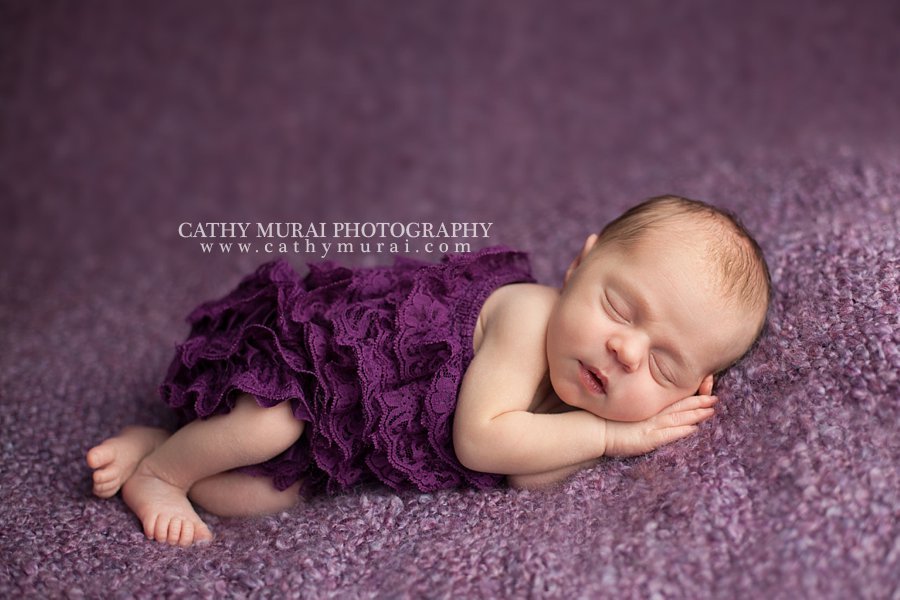 Precious Newborn Baby Girl, wearing a purple lace romper, posing on the bean bag beanbag with purple throw cover, Los Angeles. Pasadena, Newborn photographer, Cathy Miurai Photography 
