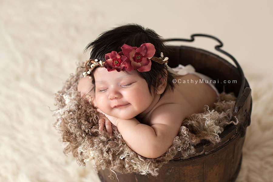 6 weeks old baby newborn baby girl wearing a red flower hair garland, smiling and posing chin on the wrists, Captured by Los Angeles, Alhambra Newborn Photographer, Cathy Murai Photography