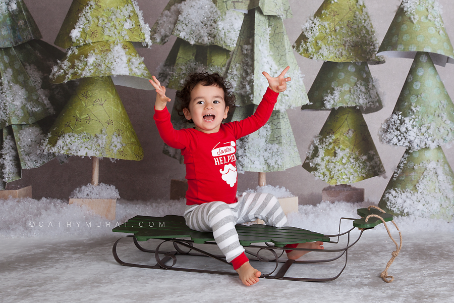 A happy boy wearing christmas pajama sitting on the sleigh in frotnt of the christmas trees by lemon backdrop stop Cathy-Murai-Photography- Alhambra-South Pasadena-Pasadena-San Marino-San Gabriel Valley-Los Angeles-studio photography-Professional Christmas Photographer-Professional Christmas Photography, Christmas portrait photography Professional Christmas Photographer, Professional Christmas Photography, Children Christmas portrait photography, Christmas children photography, Christmas kids photography ideas, Christmas kids pictures