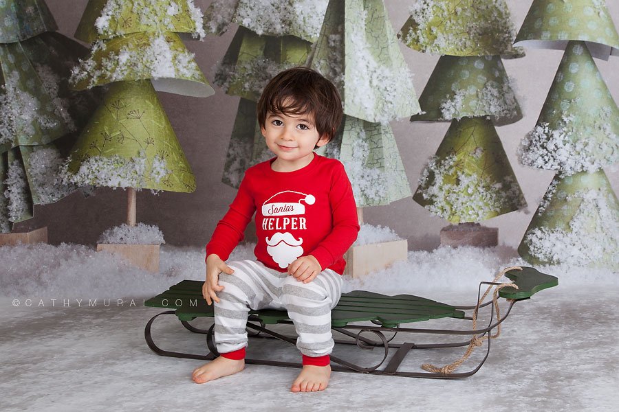 A handsome boy wearing christmas pajama sitting on the sleigh in frotnt of the christmas trees by lemon backdrop stop Cathy-Murai-Photography- Alhambra-South Pasadena-Pasadena-San Marino-San Gabriel Valley-Los Angeles-studio photography-Professional Christmas Photographer-Professional Christmas Photography, Christmas portrait photography Professional Christmas Photographer, Professional Christmas Photography, Children Christmas portrait photography, Christmas children photography, Christmas kids photography ideas, Christmas kids pictures