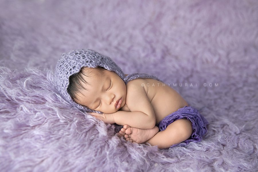 Sleeping Asian newborn baby girl wearing a purple lace bloomer and bonnet posing  on the purple lavender flokati rug background. Captured by Cathy Murai Photography, Los Angeles Newborn Photographer, Alhambra Newborn Photographer, San Gabriel Newborn Baby Photographer, newborn props, newborn photography props.