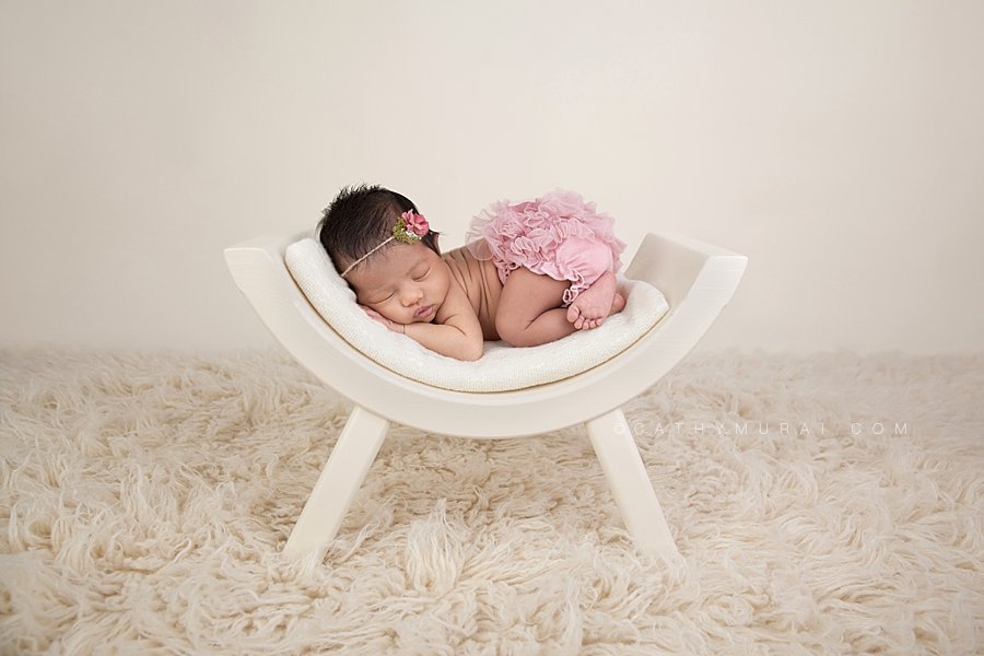 Asian baby girl wearing pink bloomer / diaper cover and pink flower headband sleeping and posing on the cream color curved bench (newborn prop, photography prop, newborn photo prop created by  Mr. & Mrs. And Co. on cream flokati rug.. Captured by Cathy Murai Photography, San Gabriel Valley, Newborn Photographer, Alhambra Newborn Photographer, Pasadena Newborn Photographer, Los Angeles Newborn Photographer