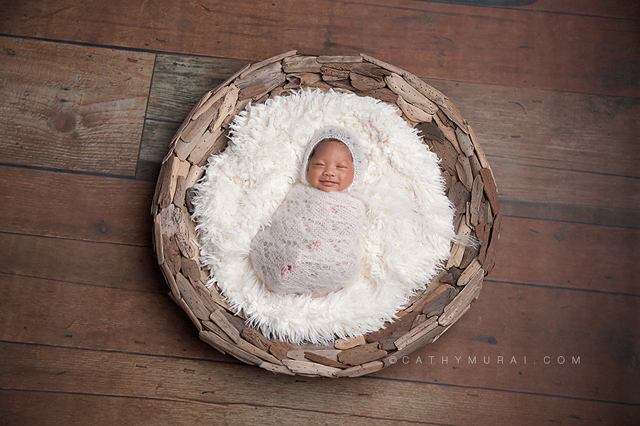 preemie newborn baby at 5 weeks old, wearing white knit hat and wrap, smiling while sleeping on wooden puzzled basket on the wood floor, captured by los angeles newborn baby photographer, los angeles preemie photographer, los angeles newborn photographer, alhambar newborn baby photographer, lalhambra preemie photographer, alhambra newborn photographer, studio newborn photographer, Cathy Murai Photography
