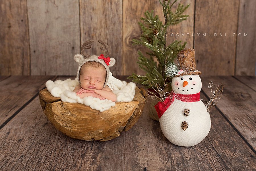 Christmas Baby. Christmas Newborn baby girl wearing a reindeer hat is posed in the wooden bowl next to the snowman and Christmas tree. Orange County Newborn Photographer based in Irvine - Cathy Murai Photography
