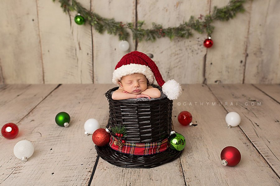 Christmas Baby. Christmas Newborn baby girl wearing a red Santa hat is posed in the snowman hat surrounded by Christmas ornaments. Orange County Newborn Photographer based in Irvine - Cathy Murai Photography