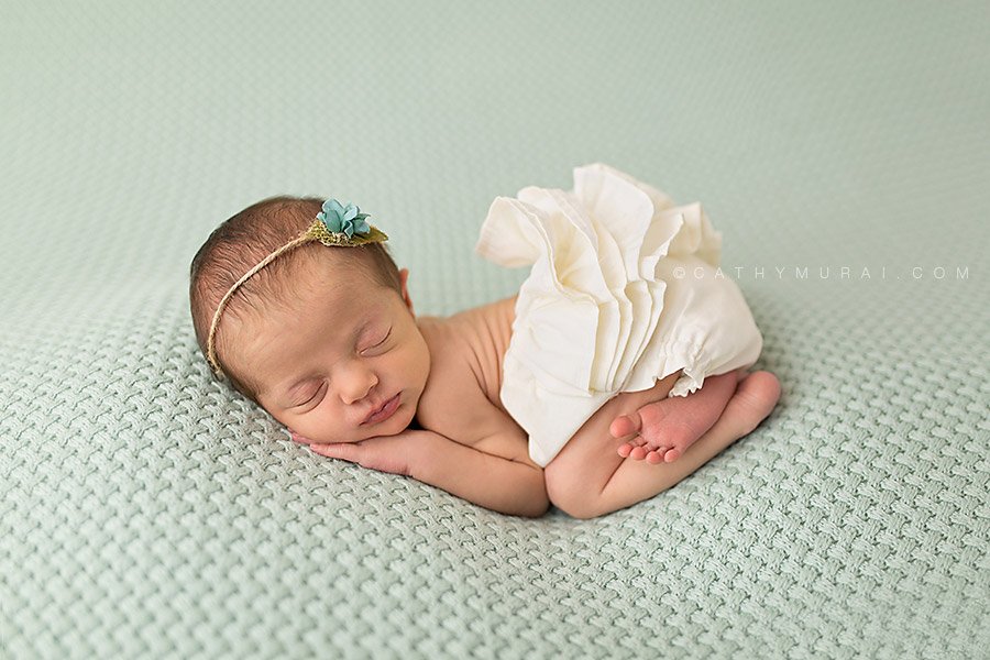 Newborn baby girl wearing teal headband and white diaper cover posed on the teal backdrop. Irvine, Orange County Newborn photography, newborn portraits, newborn photo.  