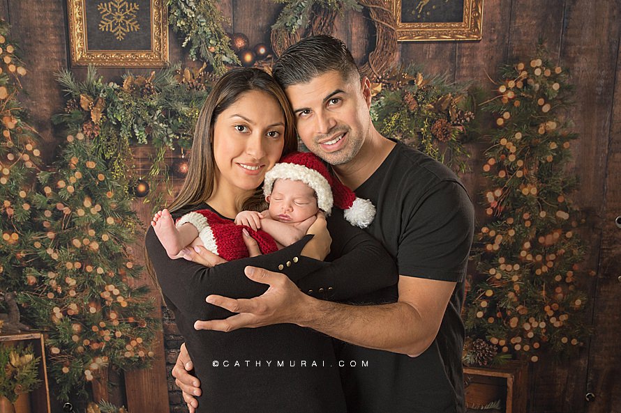 Newborn Session and Birth Announcement Photographs - Orange County Newborn Photographer - Cathy Murai Photography - photography studio based in Irvine, CA. Newborn baby boy wearing Santa prop / outfit in his parents' arms during his newborn session. Newborn family portrait, Newborn Holiday photo, Christmas baby, Newborn Christmas picture, Baby Dream backdrop - Warm Wishes, Santa Baby, Christmas Baby, newborn and family photography, newborn and family photo, newborn and family posing, newborn and family portrait