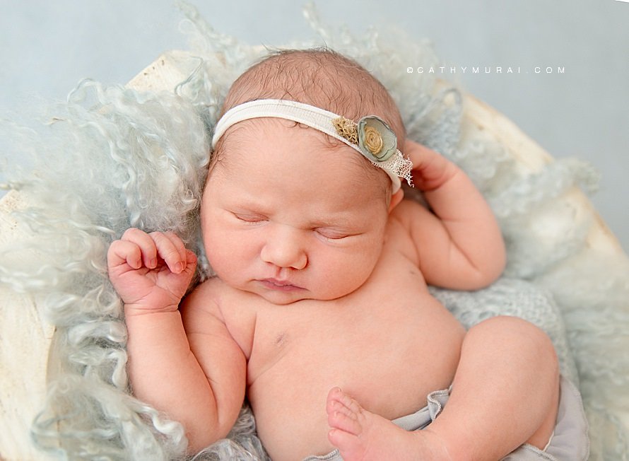 Cathy Murai Photography is a Irvine Newborn photographer based in Orange County, CA. This adorable newborn picture was captured in her Irvine Newborn Photography studio. Newborn baby girl sleeping in a white bowl with a light blue curl blanket prop. 