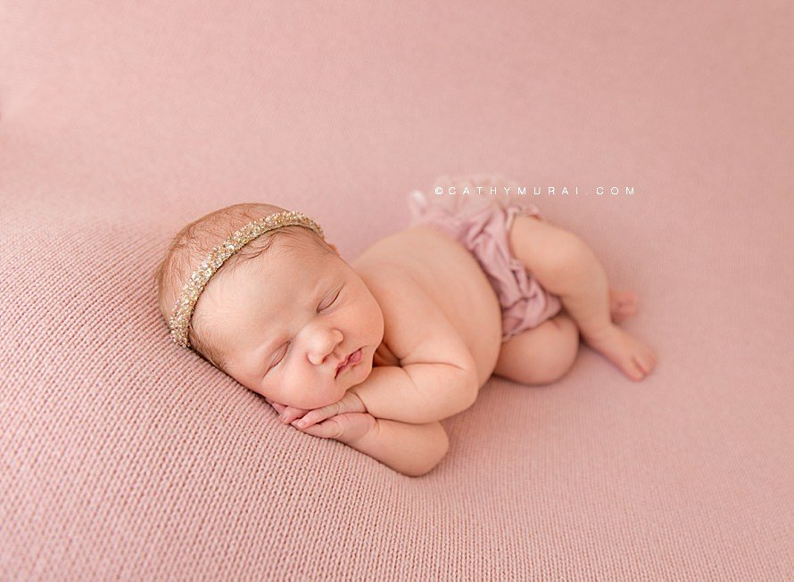 Cathy Murai Photography is a Irvine Newborn photographer based in Orange County, CA. This adorable newborn picture was captured in her Irvine Newborn Photography studio. Newborn baby girl wearing a pink beads headband and pink blush raffle diaper cover, posing side lay pose while she was sleeping on the blush pink backdrop blanket during her newborn session in Irvine, CA.