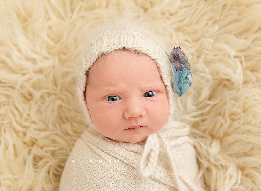 Cathy Murai Photography is a Irvine Newborn photographer based in Orange County, CA. A widely awake newborn baby girl wearing a cream bonnet in a simple swaddle pose.  This adorable awaken newborn picture was captured in a Irvine Newborn Photography studio