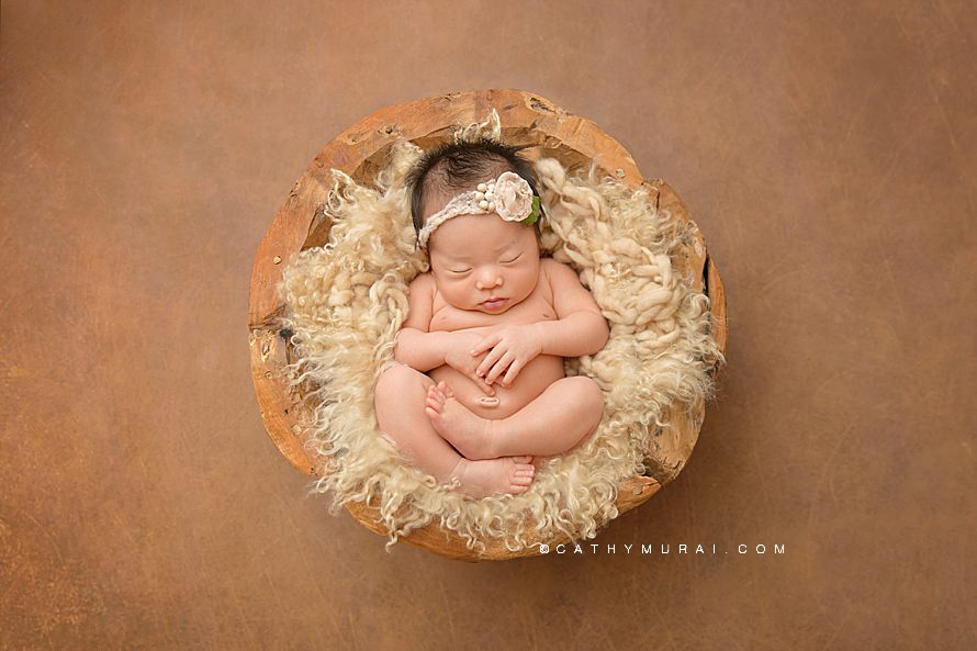 Natural Organic Newborn Photography Session by Cathy Murai Photography, Orange County Newborn and baby photographer in Irvine, a newborn baby girl wearing a pink headband is in a wooden bowl newborn photography prop, on Intuition Background