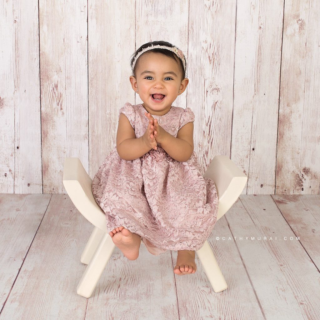 Happy first birthday girl on a cream curved wooden chair during her first birthday photoshoot by Cathy Murai Photography, a Irvine baby photographer