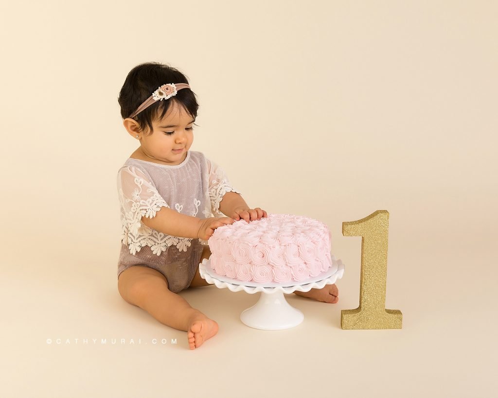 First Birthday Cake Smash Photography with a vintage style using a pink cake, white cake stand, and a gold number one prop by Cathy Murai Photography, a Irvine baby photographer