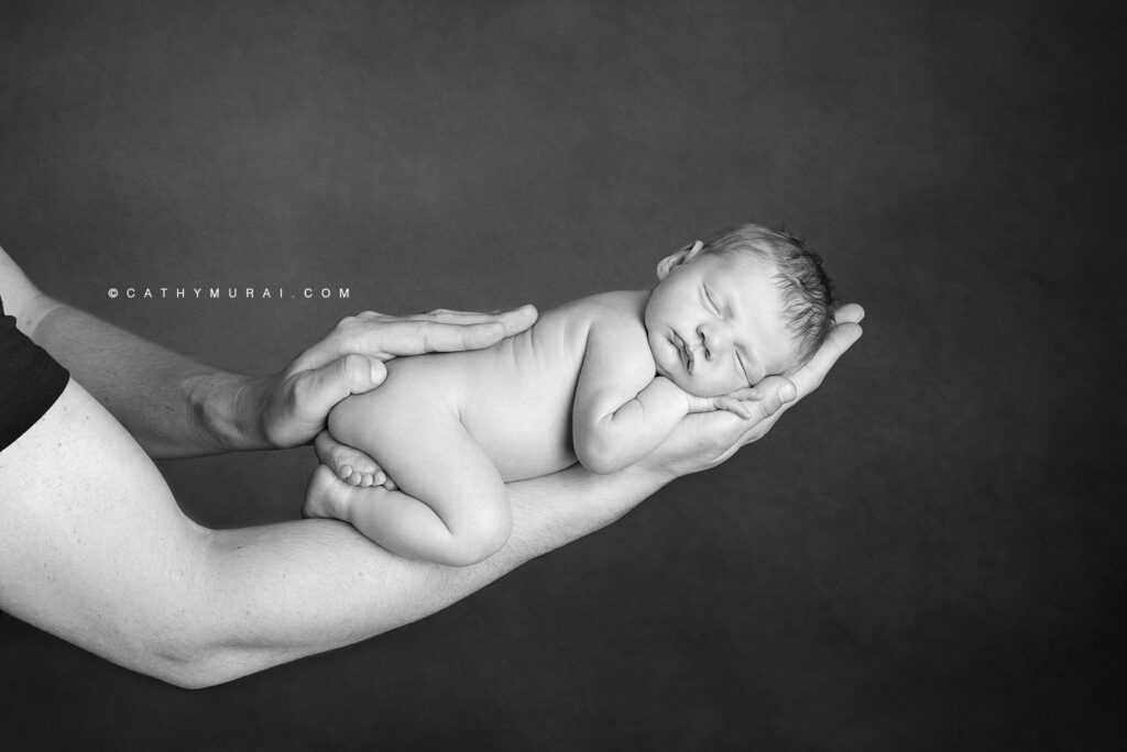 Black and white photo of newborn baby with daddy's arms.