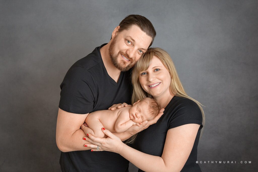 10-day old baby Finn is photographed with his parents. Dad is holding Finn in his arm. Both parents are smiling at the camera for their first family portrait.