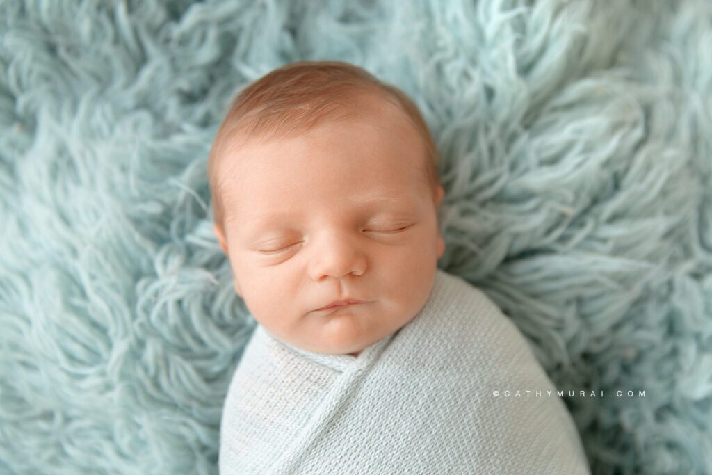 Sleeping newborn baby wrapped in a teal soft swaddle