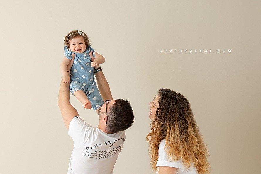 A candid shot of a family portrait in the studio while a daddy holding his happy smiling baby girl up in the air