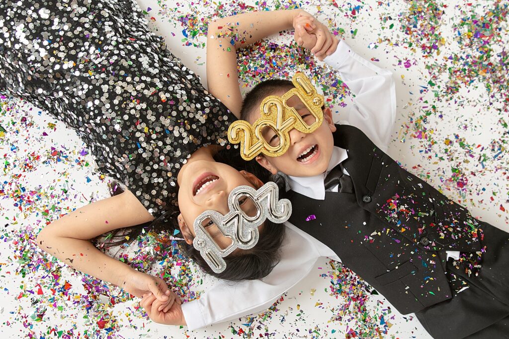 Fun and colorful New Year photo shoot with Confetti - Portrait Studio in Orange County, California. 

Happy new year photoshoot photo ideas
Happy New year photoshoot ideas kids 

Happy New Year! 2021!  A girl wearing a black metallic dress and a boy wearing a black vest and tie are celebrating New Year with 2021 eye glasses and metallic colorful confettis around them.  
