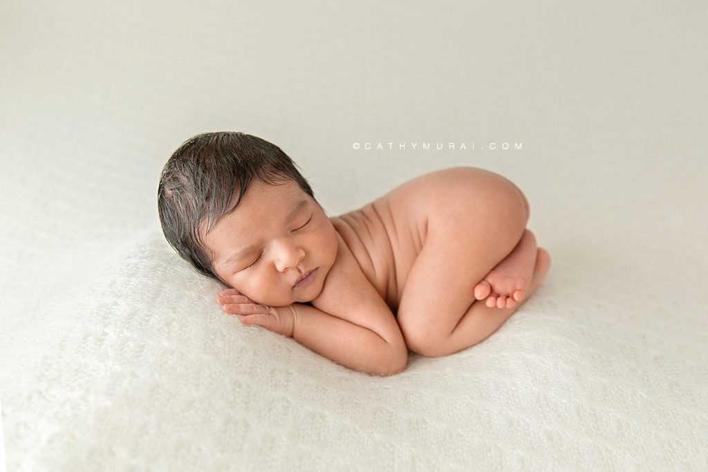 Newborn baby boy curled up sleeping on a white blanket during his newborn photo session with Cathy Murai Photography, orange county newborn photographer, in her studio in Irvine
