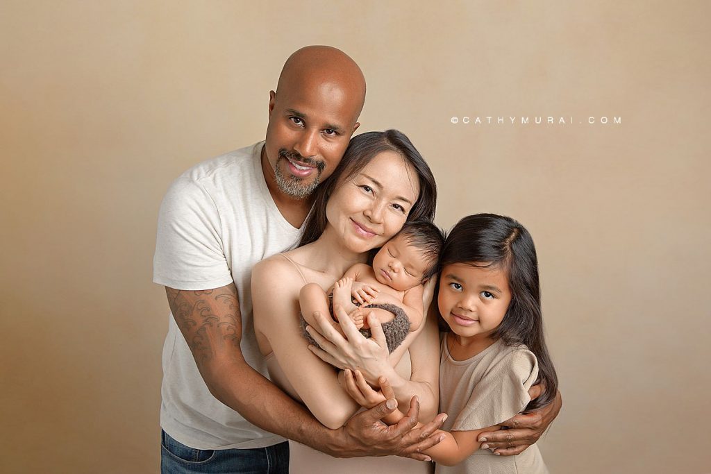 Family of mom, dad, sister, and baby brother smile softly at the camera while wearing cream and beige for their Newborn Family Photos with Cathy Murai Photography - Orange County Newborn Photographer in Irvine, CA
